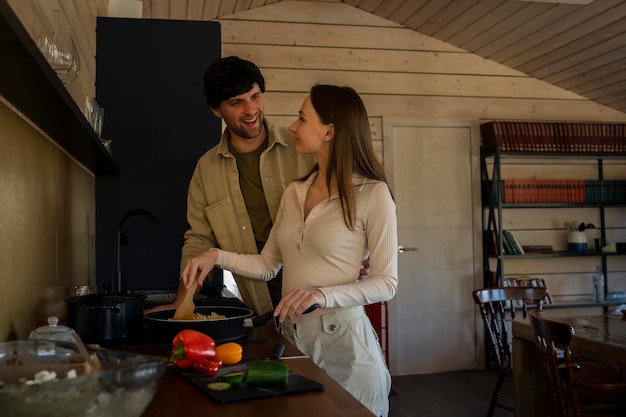 L'uomo sorridente guarda sua moglie che sta cucinando la cena sulla stufa in cucina