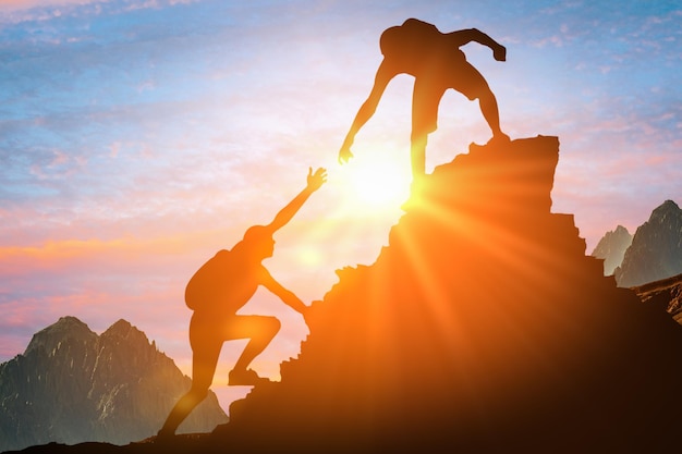 L'uomo sta dando una mano Sagome di persone che si arrampicano sulla montagna al tramonto Concetto di aiuto e assistenza Sagome di due persone che si arrampicano sulla montagna e aiutano