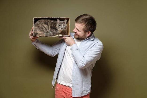 L'uomo sta giocando con il suo adorabile gatto che si è arrampicato in una scatola di cartone e sembra sconcertato