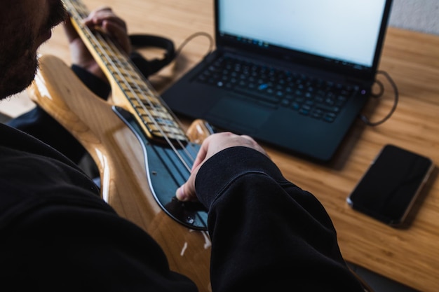 L'uomo sta imparando a suonare la chitarra con gli auricolari e il laptop