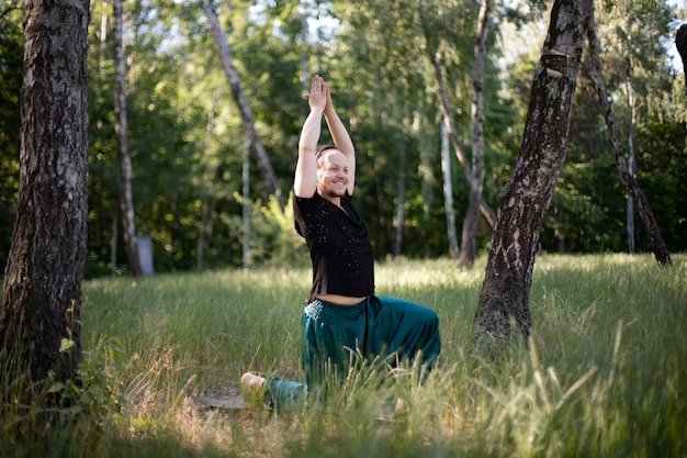 L'uomo sta in un'asana che fa yoga nel parco sull'erba verde. Giornata Internazionale dello Yoga