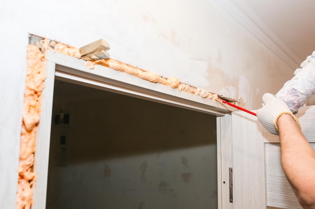 L'uomo sta installando la porta con una schiuma spray Lavori di riparazione Manutenzione nell'appartamento