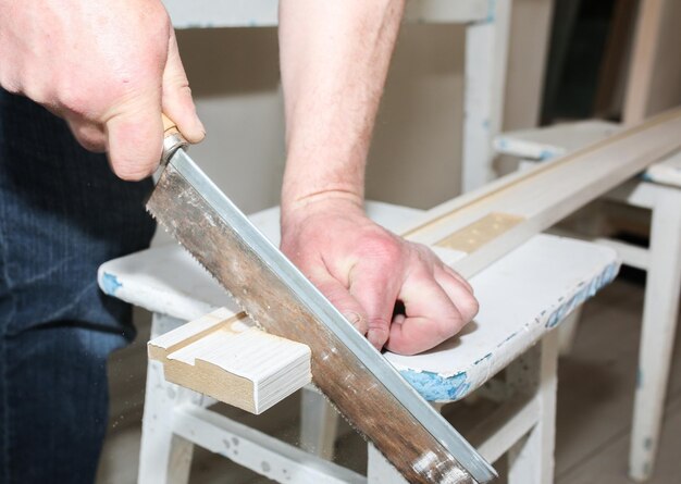 L'uomo sta installando le porte. Carpentiere che sega la plancia di legno. Lavori di riparazione. Manutenzione in appartamento.