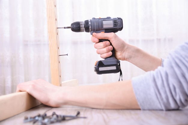 L'uomo sta lavorando con l'assemblea della mobilia facendo uso del cacciavite elettrico nell'installazione della nuova casa - lavoro in loco del tecnico facendo uso del concetto degli attrezzi per bricolage