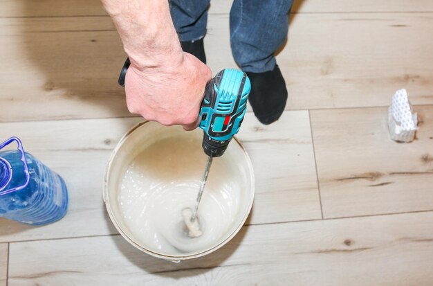 L'uomo sta mescolando la colla spackling nel secchio Carta da parati appesa nell'appartamento Restauro all'interno Lavori di ristrutturazione