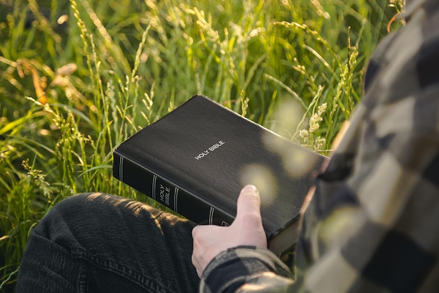L'uomo sta tenendo la Sacra Bibbia in un campo durante il concetto di tramonto per la fede, la spiritualità e la religione