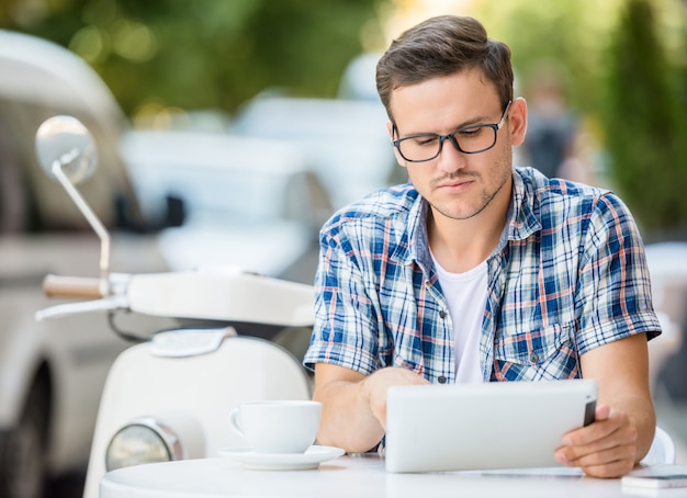 L'uomo sta usando la tavoletta digitale mentre era seduto nel caffè sul marciapiede.