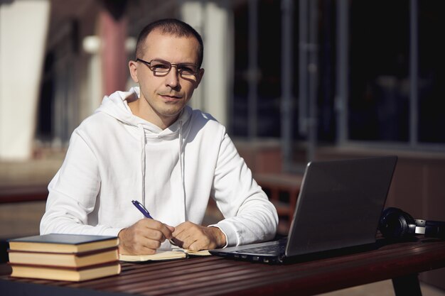 L'uomo studia su laptop e scrive su un notebook mentre è seduto per strada a un tavolo