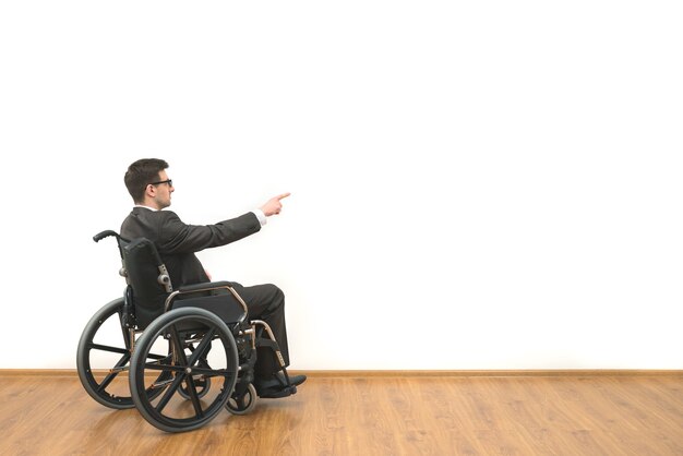 L'uomo su una sedia a rotelle che gesticola sullo sfondo del muro bianco