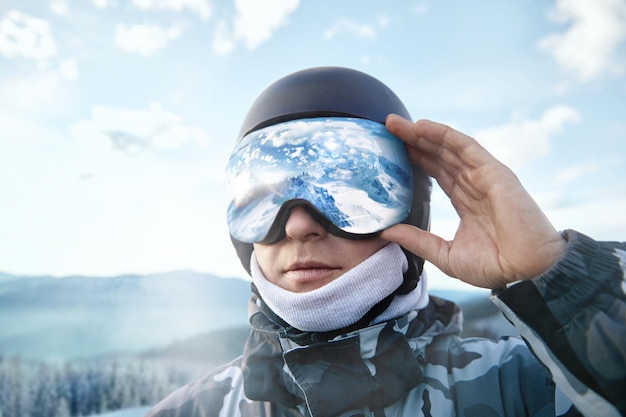 L'uomo sullo sfondo del cielo blu tiene gli occhiali da sci con il riflesso delle montagne innevateInverno