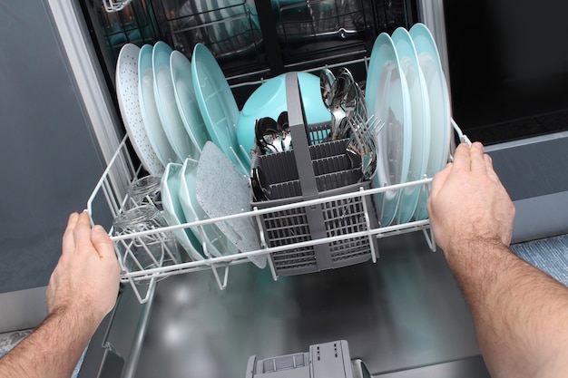 L'uomo svuota la lavastoviglie in cucina. Primo piano delle mani maschili che caricano i piatti nella lavastoviglie