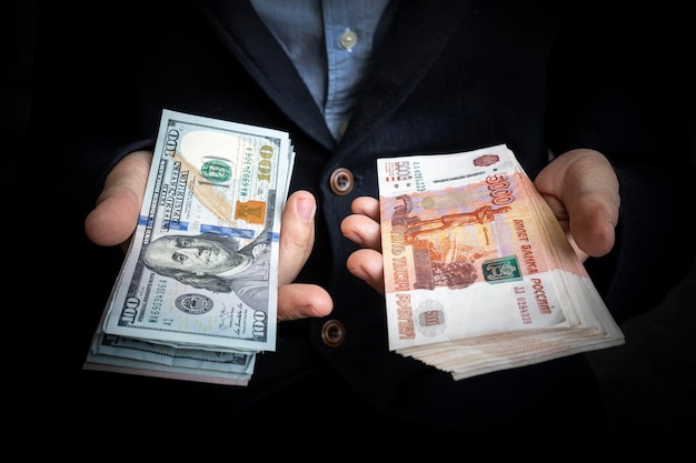 L'uomo tiene in mano dollari americani e rubli russi Il concetto di scegliere una valuta per gli insediamenti internazionali il confronto dei pagamenti internazionali tra l'economia russa e quella statunitense