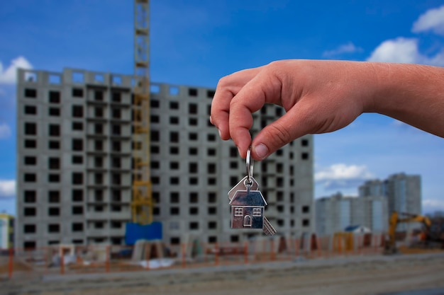 L'uomo tiene in mano le chiavi di casa sullo sfondo di un edificio a più piani. Concetto per l'acquisto e l'affitto di appartamenti.