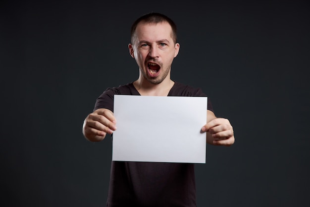 L'uomo tiene in mano un foglio di carta per poster vuoto. Sorriso e gioia, posto per il testo, copia spazio