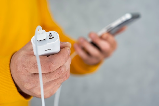 L'uomo tiene in mano uno smartphone e un caricabatterie portatile su uno sfondo grigio. Power Bank ricarica il telefono.