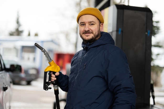 L'uomo tiene la pompa del carburante mentre rifornisce di carburante la sua auto alla stazione di servizio quando fa freddo