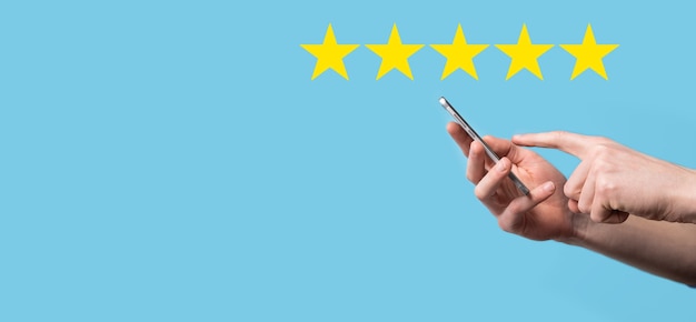 L'uomo tiene lo smart phone in mano e dà una valutazione positiva, icona simbolo a cinque stelle per aumentare la valutazione del concetto di azienda su sfondo blu.