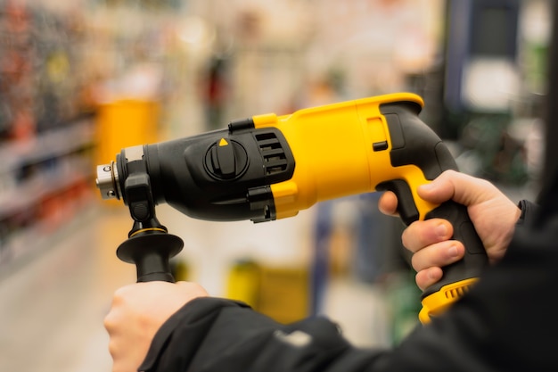 L'uomo tiene un perforatore giallo per i lavori di riparazione nelle sue mani sullo sfondo di vetrine in un negozio di ferramenta.