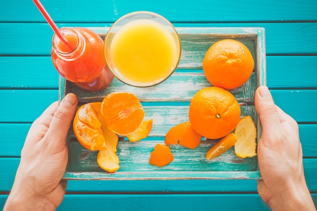 L'uomo tiene un vassoio vintage con mandarini e succo di frutta fresco nelle sue mani