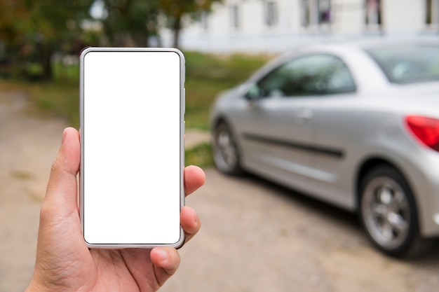 L'uomo tiene uno smartphone con schermo vuoto nella mano sinistra vicino al veicolo parcheggiato. La persona in strada utilizza l'applicazione di collegamento auto sul telefono cellulare. Avvio remoto del motore utilizzando l'app del telefono. Avvio computer di bordo.