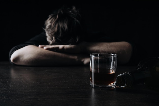 L'uomo tossicodipendente depresso e ubriaco alcolico si trova davanti al bicchiere di whisky