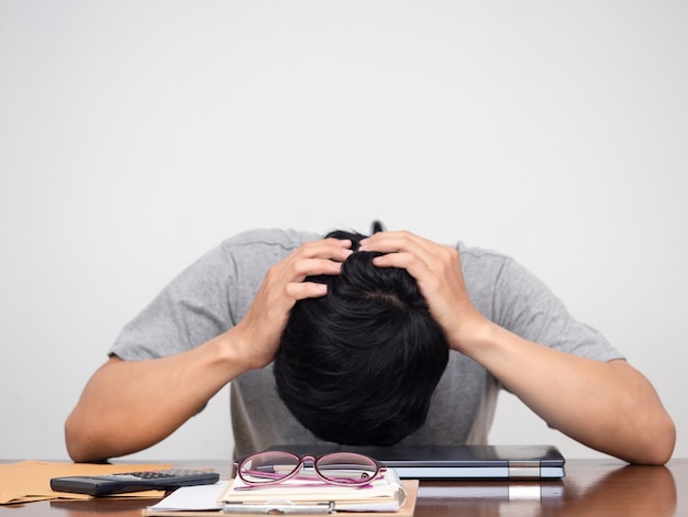 L'uomo triste che tiene la testa si siede sul fondo bianco della tavola del posto di lavoro