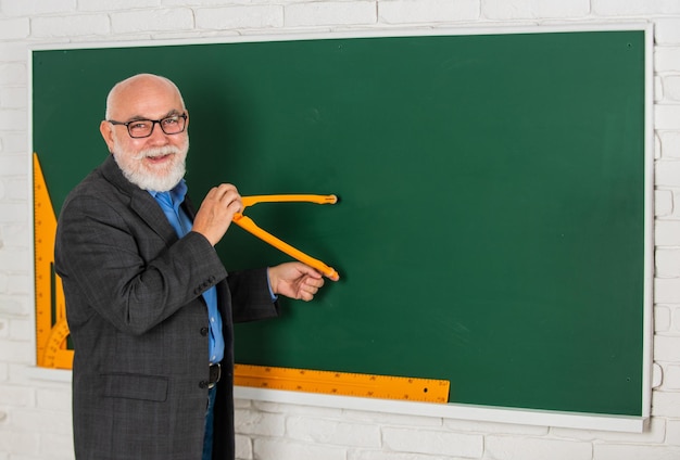 L'uomo tutor barbuto disegna con la bussola sulla lavagna Torna a scuola Concetto di strumenti grafici matematici Verso la conoscenza studia la matematica per ottenere buoni risultati insegnante uomo anziano usa lo spazio della copia dello strumento bussola