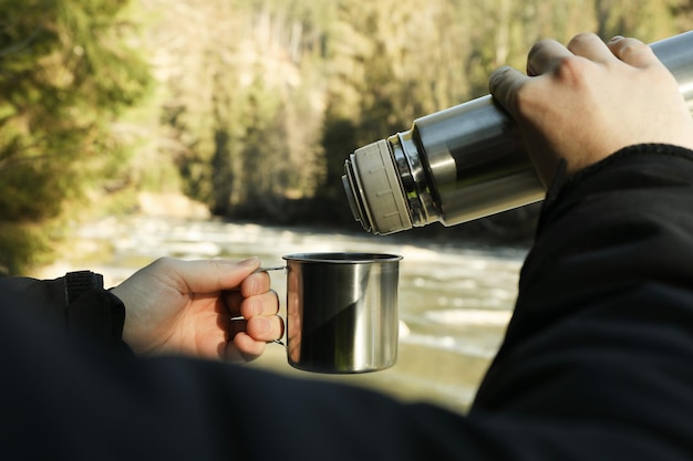 L'uomo versa la bevanda dal thermos alla tazza all'aperto