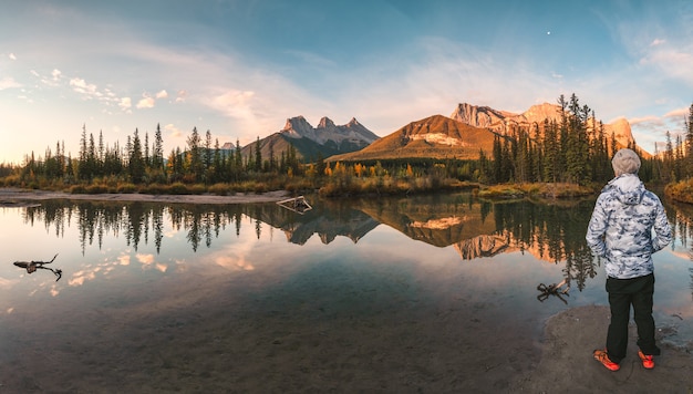 L'uomo viaggiatore in piedi gode del paesaggio delle montagne delle tre sorelle riflesso sul fiume in autunno a Canmore, Canada