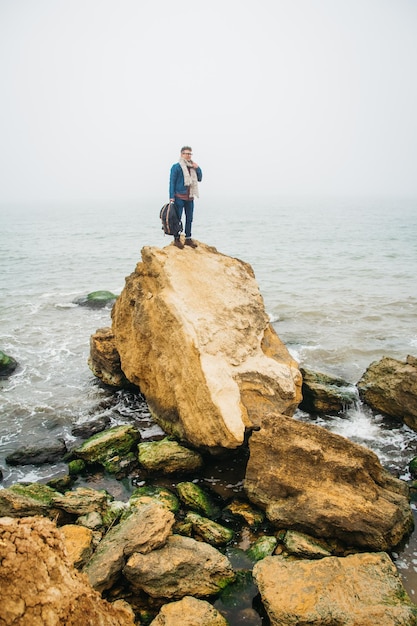 L'uomo viaggiatore si erge su una roccia sullo sfondo di un bellissimo mare. Posto per testo o pubblicità