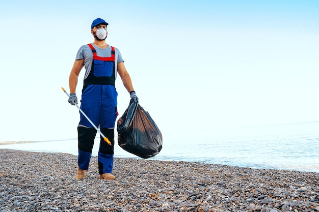 L'uomo volontario raccoglie immondizia sulla spiaggia con un bastone estensore di portata