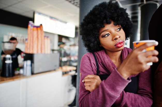 L'usura della donna dell'afroamericano dei capelli ricci sul maglione ha proposto al caffè dell'interno con la tazza di tè o di caffè.