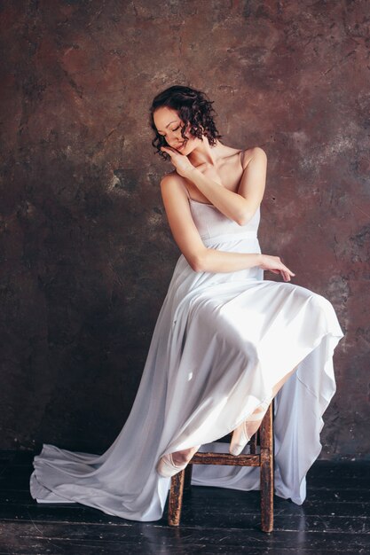 La ballerina del ballerino di balletto in bello vestito bianco volante sottile sta posando nello studio scuro del sottotetto