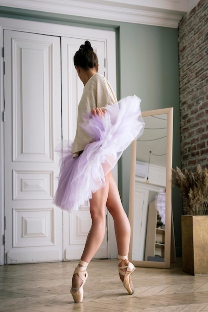 La ballerina posa mostrando le gambe nella stanza davanti allo specchio in scarpe da punta e tutù