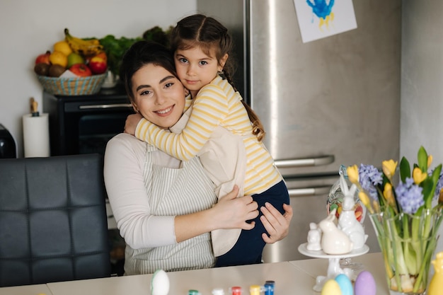 La bambina abbraccia sua madre mentre dipingono le uova di pasqua in cucina