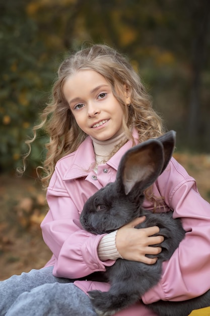 La bambina abbraccia un gigantesco coniglio grigio nella foresta autunnale Concetto amore per la natura e amore per gli animali