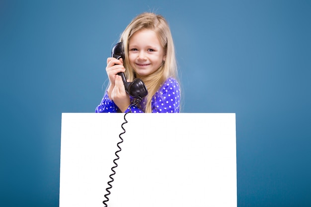 La bambina adorabile in vestito viola tiene il cartello e il microtelefono in bianco vuoti