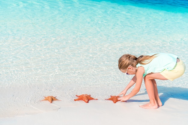 La bambina adorabile si diverte alla spiaggia tropicale durante la vacanza