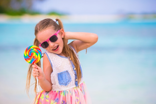 La bambina adorabile si diverte con la lecca-lecca sulla spiaggia