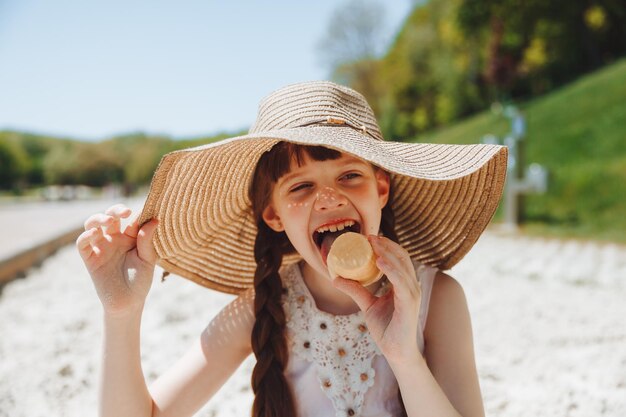 La bambina affascinante con un cappello mangia il gelato sulla spiaggia della spiaggia Concetto di vacanza estiva