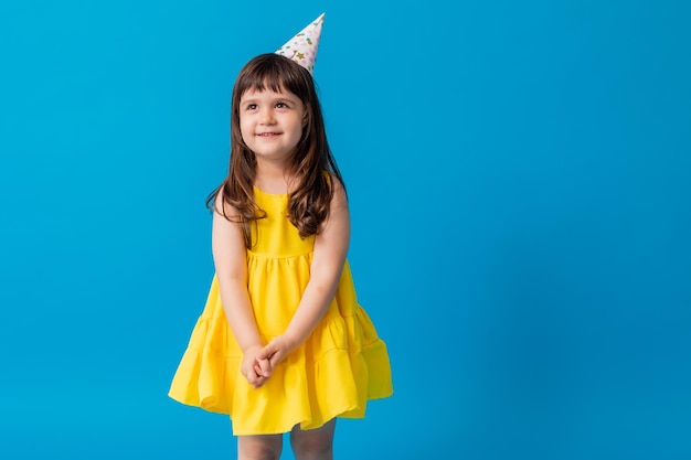 La bambina affascinante in un vestito giallo su sfondo blu lancia coriandoli colorati Compleanno