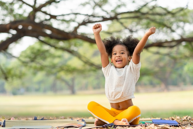 La bambina afroamericana felice che sorride e solleva la sua mano mentre si siede nel parco