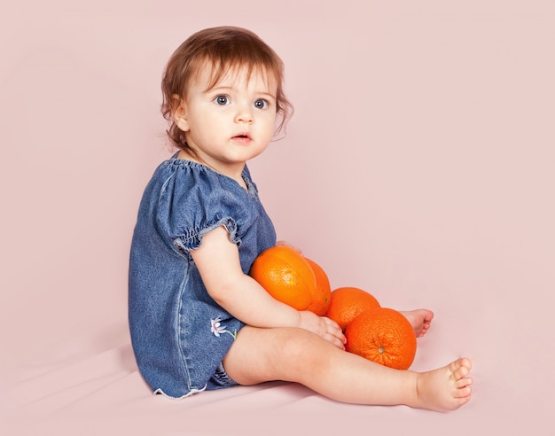 La bambina alla moda vestita con l'arancia sta posando nello studio sul rosa