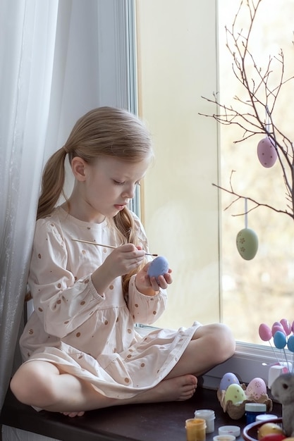 La bambina allegra dipinge le uova per le vacanze di Pasqua Buona Pasqua