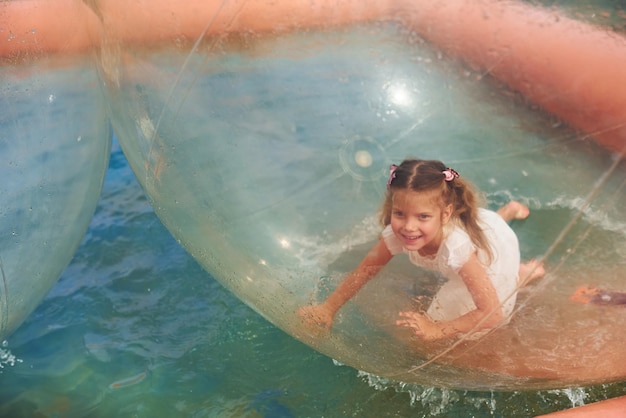 La bambina allegra si diverte all'interno della palla da passeggio galleggiante dell'acqua