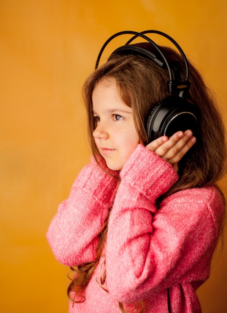 la bambina ascolta musica con le cuffie su uno sfondo giallo