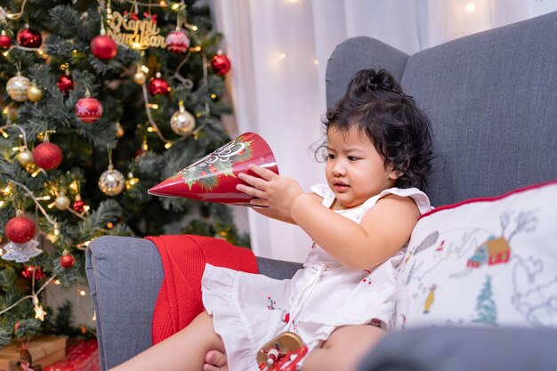 La bambina asiatica felice si diverte il giorno di Natale. Bambino con genitore con decorazione dell'albero di Natale a casa in vacanza.