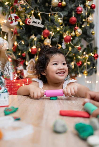 La bambina asiatica felice si diverte il giorno di Natale. Bambino con genitore con decorazione dell'albero di Natale a casa in vacanza.