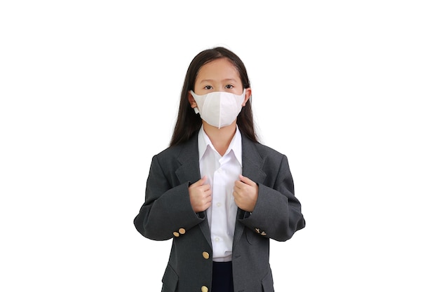 La bambina asiatica indossa una camicia da cerimonia, una tuta da studente e una maschera protettiva che indossa e tiene le mani tenendo la tuta in posa isolata su sfondo bianco