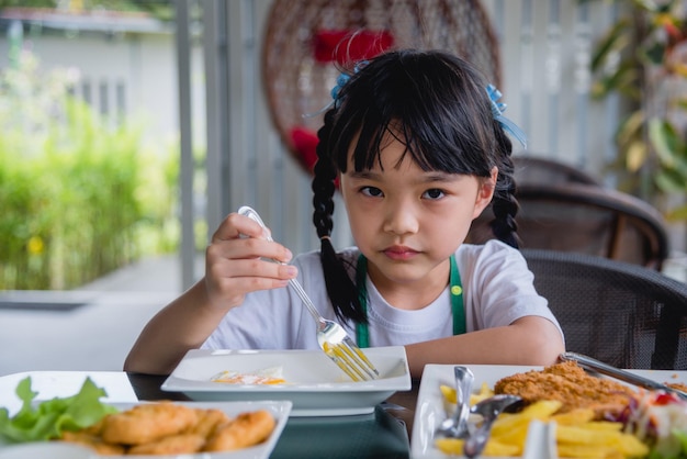La bambina asiatica mangia l'uovo fritto sul piatto al tavolo